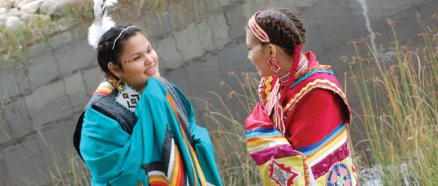 Photo of two teen First Nations girls dressed in traditional indigenous outfits.