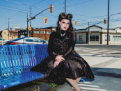 Betty Baker on a bright blue metal bench with street intersection in the background.